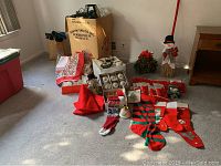 Photo showing various Christmas decorations including stockings, a snowman broom decoration, several holiday candles, a box of silver and white ball ornaments, and some linens.