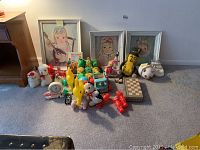 Full lot showing three framed pictures of girls, plush toys, dolls, toy truck, yellow pull toy, and chess set arranged on carpet.