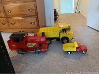 Photo showing red toy train engine in front, large yellow Mighty Dump truck in back, and smaller red-yellow Tonka truck arranged on carpeted floor.