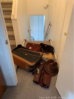 All items scattered on floor at bottom of stairs: two suitcases, purse, garment bag, men's hat