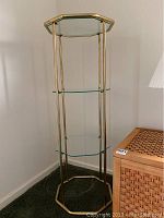 Full view of the three-tier glass and metal etagere standing in a corner against light-colored walls.