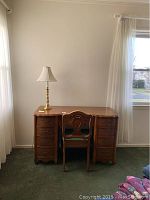 Desk with chair and brass lamp on top, shown in a room near window with curtains