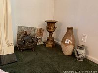 Unframed reproduction print, ceramic urn, vases, and ship sculpture arranged on floor for display