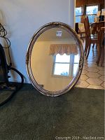 Full view of the Carolina Mirror Company oval wall mirror, showing the gold-toned ornate frame and reflective glass.