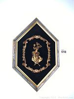 Full view of diamond-shaped framed wall art with gold Rococo style figure set on black velvet background