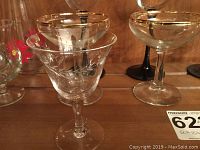 Photo showing clear crystal aperitif glasses with etched designs and gold-rimmed bowls. Some glasses have clear stems, others have black stems.