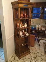Full view of tall wooden display cabinet with glass shelves inside and various display items placed on the shelves. Cabinet features clear glass door and decorative trim.