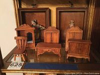 Wooden dollhouse furniture including chair, mirror, armoire, desk, bench, cabinet and two boxed musical figurines visible behind.