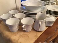 View of cups, creamer, sugar bowl, and stacked plates and bowls on table showing pattern and quantity.