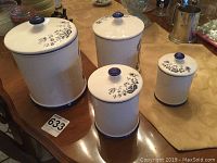 Four Heritage canisters shown with lids on a table, each varying in size with floral patterns and navy blue accents.