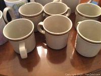 Six stoneware coffee mugs from Old Brook Collection arranged with other assorted mugs on a table.