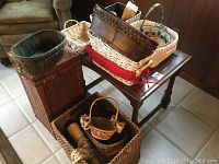 Overview showing several wicker and wooden baskets stacked on a hardwood side table and the floor.