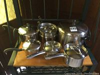 Full set of six stainless steel pots with lids displayed on wooden shelf, showing variety of pot sizes including steamer and crock pots.