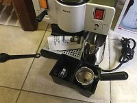Krups Espresso Plus machine with portafilter, accessories, power cord visible on tile floor
