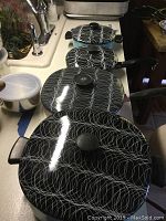 Four pieces of enamel cookware including pots and pans with black and white circular patterned exterior, black handles and lids with knobs taken on kitchen counter.