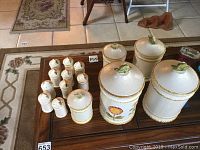 Set of 8 ceramic canisters of varying sizes with white textured finish and floral decorations alongside 8 matching salt and pepper shakers.