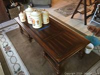 Full view of the dark brown rectangular wooden coffee table with panel top and some decorative canisters placed on it, showing general condition and style.