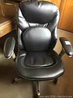 Front view of black leather desk chair showing padded backrest, seat, and armrests on wheeled base.