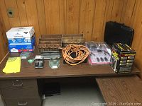 Lot items arranged on tabletop with wooden and metal desk caddies, extension cord, scale, briefcase, screwdrivers, hole punchers, and boxed heater.