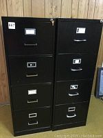 Two black four-drawer filing cabinets standing side by side, each with locking keys on top.