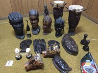 Photo showing arrangement of various hand carved wood busts, masks, small figurines, and drums on the floor.
