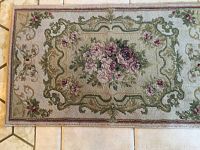 Smaller beige floral area rug with pink rose floral centerpiece and decorative border on tile floor.