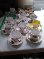 Photo shows a mix of 12 bone china tea cups and saucers with varied floral patterns and some gold trim, arranged on a white table.