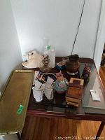 Overview of the lot showing the copper pitcher, large conch shell, oil lamp, ceramic monks, and other decorative items on dark glass table.