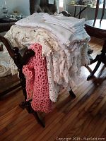 Photo of wood quilt rack with folded vintage linens draped over it, showing details of crocheted and embroidered fabric pieces.