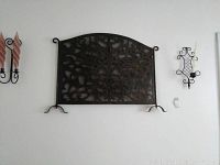 Front view of black cast iron fire grate mounted on wall with two black metal wall sconces on either side, holding twisted pink taper candles.
