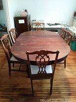 Full view of the oval antique wooden dining table with six chairs with fabric upholstered seats around it, wood surface visible with some wear marks.