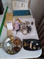 Photo showing a tray with assorted brooches, rings, earrings, pendants, a gold brick jewelry box, and blue jewelry organizer with rings.