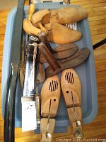 Collection of wooden and metal shoe trees with several shoe horns on top of blue plastic storage bin