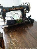 Antique Davis Rotary black sewing machine with gold decorative lettering, placed on wooden surface. Several boxes and manual visible on top of machine.