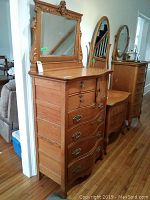 Front left angle view of oak highboy and swing mirror showing carved crest, drawers, and cabinet door