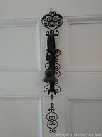 Full frontal view of the vintage cast iron pull chain bell mounted on white door, showing ornate heart and scroll design on the bracket, with bell hanging below and pull chain with decorative end.