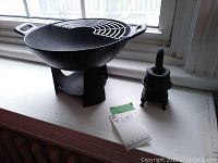 Photo showing small cast iron wok on its stand next to miniature cast iron stove and tape measure for scale.