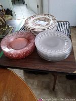 Stacked Johnson Bros turkey plates behind piles of clear glass apple-shaped plates and pink Depression glass bowls on a table with the striped fabric shower curtain beneath.