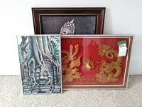 Lot displaying three framed Asian art pieces, including the Cambodian oil painting with a face and tree roots, and a wood shadow box with phoenix and dragon figures in gold on red background.