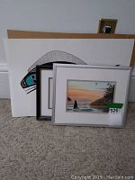 Three prints positioned side by side showing differences in matting and framing, placed on carpeted floor.