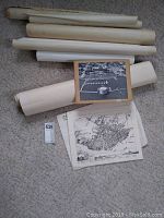 Photo showing multiple rolled charts and maps on carpet with loose maps spread, including aerial black and white photograph of waterfront and map of Kingston city.