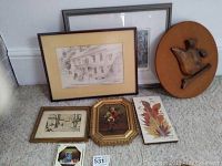 Collection of five art pieces on carpet: framed pencil sketch of house, framed monochrome landscape, floral oil painting, oil painted leaf tile, and round wooden bird plaquette.