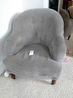 Front view of older grey upholstered armchair with tufted back and padded arms.