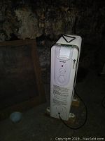 Front view of the Maxi Heat electric oil-filled radiator heater showing control panel with two knobs and an indicator light. Mounted on wooden blocks.