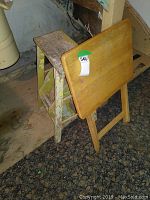 Vintage wooden folding TV table leaning against a step stool ladder, showing smooth wood surface and foldable design.