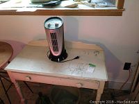 One painted wooden desk with one drawer with a Noma oscillating pillar fan placed on top, showing wear and scratches.
