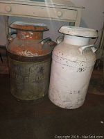 Two vintage milk cans side by side, one white painted and one rusty with Kingston Creamery embossed lettering.