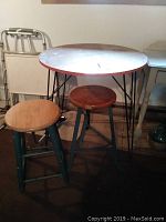 Photo showing the bistro table with round wooden top and iron frame alongside two stools with iron legs and wooden tops.