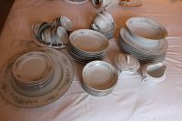 Full display of Crestwood China Montclair pattern set with all components arranged on a tablecloth. Includes stacked plates, bowls, cups, saucers, large platter, serving bowl, cream pitcher, and sugar bowl with lid.