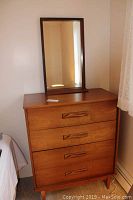 Teak dresser with four drawers closed, mirror resting on top.